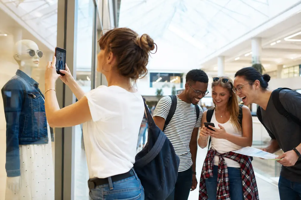 Friends photographing a mannequin in a bright shopping mall during a scavenger hunt